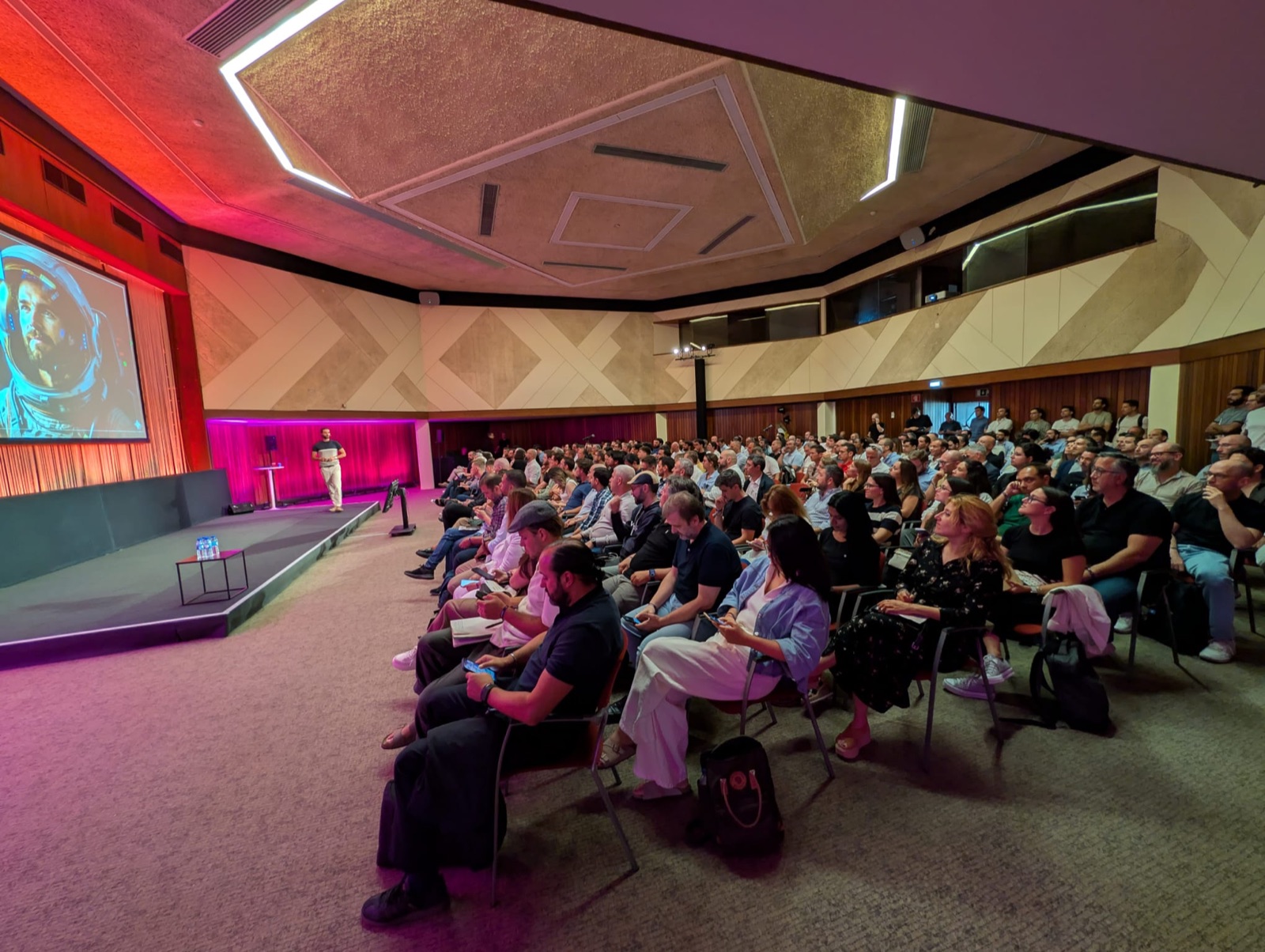 Rui Vas on a pink-lit stage at the Lisbon AI conference, seen with the seated audience