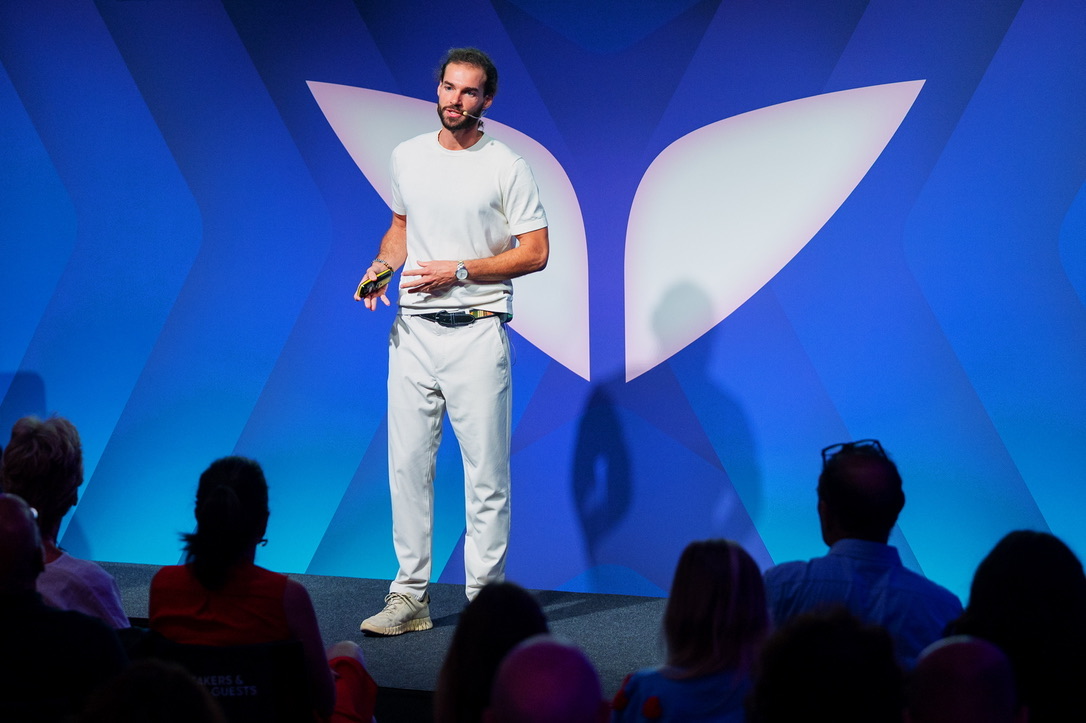 Rui Vas presenting on the blue Mindvalley stage with audience members in the foreground